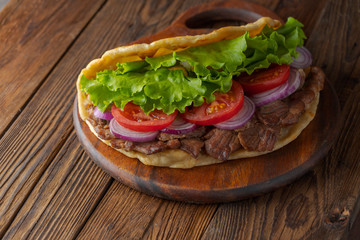 Delicious fresh homemade sandwich with chicken burspit roasted meat, tomato, onions and lettuce on wooden board on dark wooden table. Doner kebab. Healthy food concept.