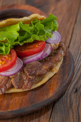 Delicious fresh homemade sandwich with chicken burspit roasted meat, tomato, onions and lettuce on wooden board on dark wooden table. Doner kebab. Healthy food concept.