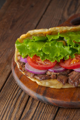 Delicious fresh homemade sandwich with chicken burspit roasted meat, tomato, onions and lettuce on wooden board on dark wooden table. Doner kebab. Healthy food concept.