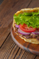 Delicious fresh homemade sandwich with chicken burspit roasted meat, tomato, onions and lettuce on wooden board on dark wooden table. Doner kebab. Healthy food concept.