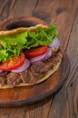 Delicious fresh homemade sandwich with chicken burspit roasted meat, tomato, onions and lettuce on wooden board on dark wooden table. Doner kebab. Healthy food concept.