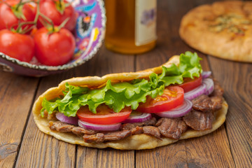 Delicious fresh homemade sandwich with chicken burspit roasted meat, tomato, onions and lettuce on wooden board on dark wooden table. Doner kebab. Healthy food concept.