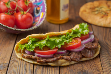 Delicious fresh homemade sandwich with chicken burspit roasted meat, tomato, onions and lettuce on wooden board on dark wooden table. Doner kebab. Healthy food concept.