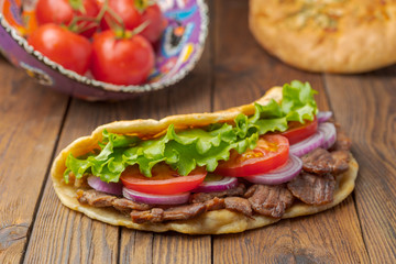 Delicious fresh homemade sandwich with chicken burspit roasted meat, tomato, onions and lettuce on wooden board on dark wooden table. Doner kebab. Healthy food concept.