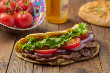 Delicious fresh homemade sandwich with chicken burspit roasted meat, tomato, onions and lettuce on wooden board on dark wooden table. Doner kebab. Healthy food concept.