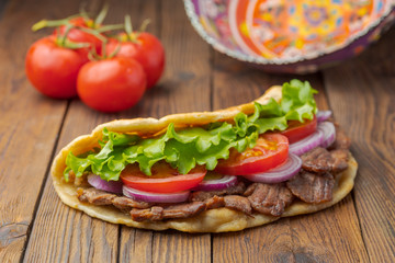 Delicious fresh homemade sandwich with chicken burspit roasted meat, tomato, onions and lettuce on wooden board on dark wooden table. Doner kebab. Healthy food concept.