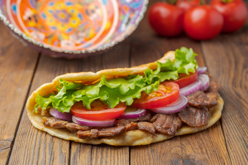 Delicious fresh homemade sandwich with chicken burspit roasted meat, tomato, onions and lettuce on wooden board on dark wooden table. Doner kebab. Healthy food concept.