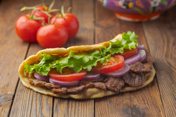 Delicious fresh homemade sandwich with chicken burspit roasted meat, tomato, onions and lettuce on wooden board on dark wooden table. Doner kebab. Healthy food concept.