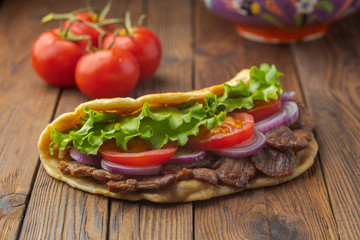 Delicious fresh homemade sandwich with chicken burspit roasted meat, tomato, onions and lettuce on wooden board on white wooden table. Doner kebab. Healthy food concept.