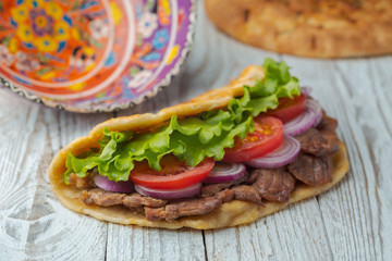 Delicious fresh homemade sandwich with chicken burspit roasted meat, tomato, onions and lettuce on wooden board on white wooden table. Doner kebab. Healthy food concept.