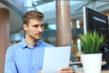 Young businessman reading paperwork at desk in office.