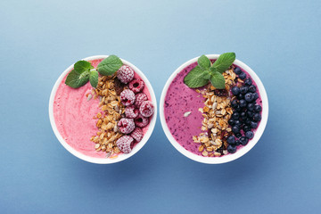 Two smoothie bowls with granola, blueberries, raspberries and mint on blue background. Healthy...