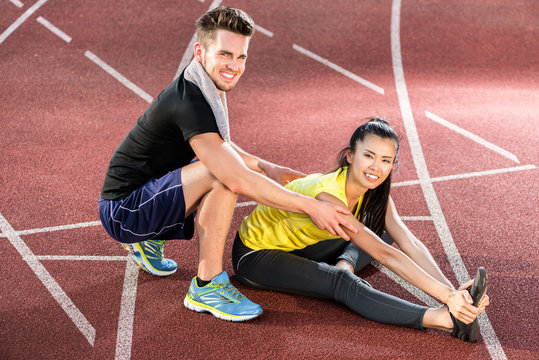 Male and female athlete doing stretching exercise together as preparation for short distance run 