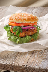 The hamburger lies on an old wooden table. On the table is a hamburger, tomato sauce, cherry tomatoes, a jar of spices.