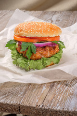 The hamburger lies on an old wooden table. On the table is a hamburger, tomato sauce, cherry tomatoes, a jar of spices.