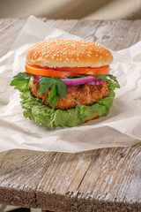 The hamburger lies on an old wooden table. On the table is a hamburger, tomato sauce, cherry tomatoes, a jar of spices.