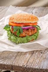 The hamburger lies on an old wooden table. On the table is a hamburger, tomato sauce, cherry tomatoes, a jar of spices.