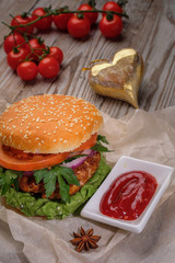 The hamburger lies on an old wooden table. On the table is a hamburger, tomato sauce, cherry tomatoes, a jar of spices.
