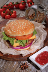 The hamburger lies on an old wooden table. On the table is a hamburger, tomato sauce, cherry tomatoes, a jar of spices.
