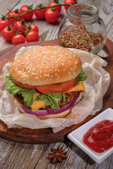 The hamburger lies on an old wooden table. On the table is a hamburger, tomato sauce, cherry tomatoes, a jar of spices.