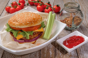 The hamburger lies on an old wooden table. On the table is a hamburger, tomato sauce, cherry tomatoes, a jar of spices.