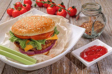 The hamburger lies on an old wooden table. On the table is a hamburger, tomato sauce, cherry tomatoes, a jar of spices.