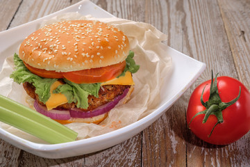 The hamburger lies on an old wooden table. On the table is a hamburger, tomato sauce, cherry tomatoes, a jar of spices.