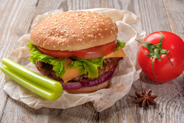 The hamburger lies on an old wooden table. On the table is a hamburger, tomato sauce, cherry tomatoes, a jar of spices.