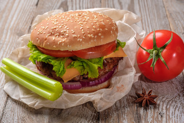 The hamburger lies on an old wooden table. On the table is a hamburger, tomato sauce, cherry tomatoes, a jar of spices.