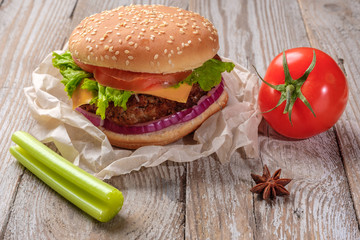 The hamburger lies on an old wooden table. On the table is a hamburger, tomato sauce, cherry tomatoes, a jar of spices.