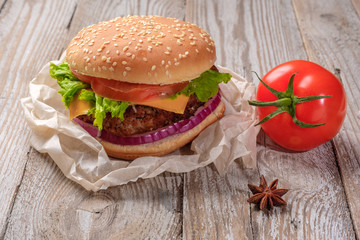 The hamburger lies on an old wooden table. On the table is a hamburger, tomato sauce, cherry tomatoes, a jar of spices.