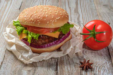 The hamburger lies on an old wooden table. On the table is a hamburger, tomato sauce, cherry tomatoes, a jar of spices.