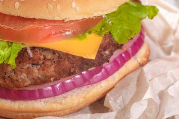 The hamburger lies on an old wooden table. On the table is a hamburger, tomato sauce, cherry tomatoes, a jar of spices.