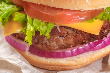 The hamburger lies on an old wooden table. On the table is a hamburger, tomato sauce, cherry tomatoes, a jar of spices.
