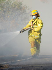 Melbourne, Australia - April 13, 2018: Fire fighter with a hose at a bush fire in an suburban area...