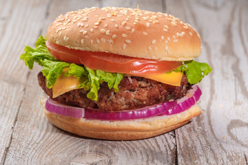 The hamburger lies on an old wooden table. On the table is a hamburger, tomato sauce, cherry tomatoes, a jar of spices.