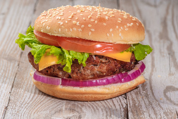 The hamburger lies on an old wooden table. On the table is a hamburger, tomato sauce, cherry tomatoes, a jar of spices.