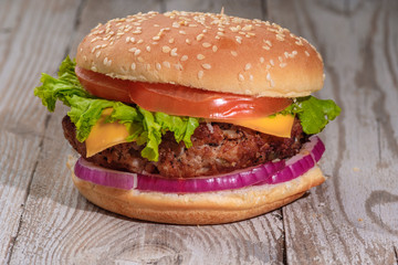 The hamburger lies on an old wooden table. On the table is a hamburger, tomato sauce, cherry tomatoes, a jar of spices.