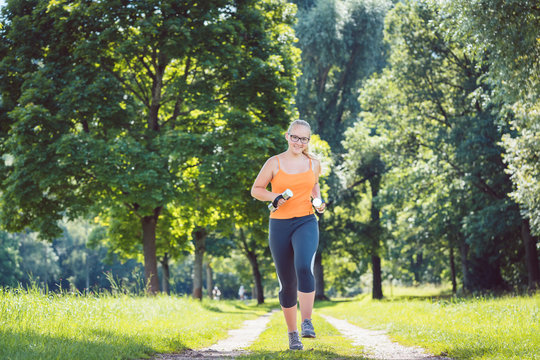Young girl running down a path on sunny meadow with weight dumbbells