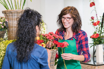 Floristin bedient freundlich lächelnd eine Kundin im Blumenladen