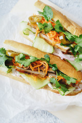 Close up of classical banh-mi sandwich with sliced grilled pork tenderloin, shredded carrots and peeled cucumbers, jalapeno peppers and cilantro on white textured background