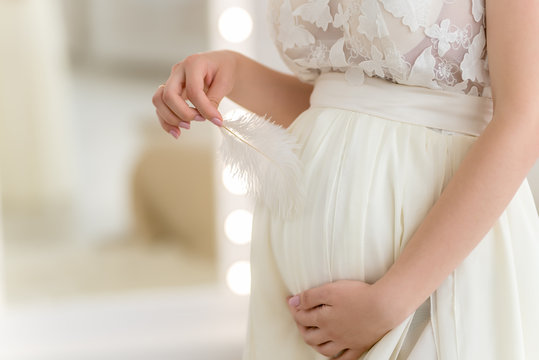 Belly of a pregnant woman holding a white feather