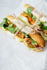Close up of classical banh-mi sandwich with sliced grilled pork tenderloin, shredded carrots and peeled cucumbers, jalapeno peppers and cilantro on white textured background