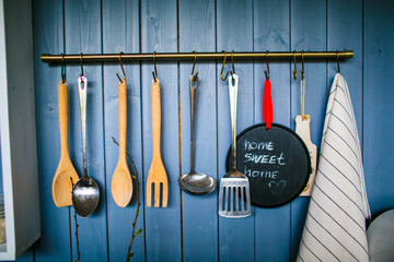 Set of wooden and metal kitchen utensils hanging on the blue wooden wall