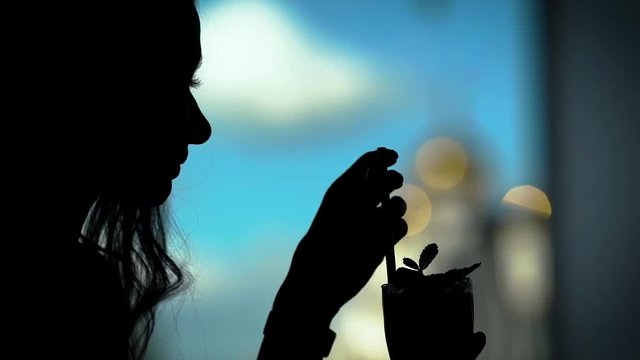 the silhouette of a woman who drinks a cocktail through a straw, the lady is in a restaurant and enjoys a drink