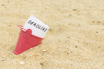 Deadline. The inscription on paper in a bucket buried in the sand.