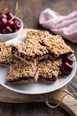 Homemade crumble bars with cherries on rustic wooden background