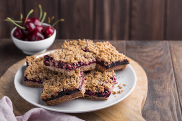Homemade crumble oatmeal bars with cherries on rustic wooden background, copy space