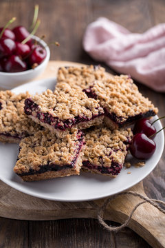 Homemade crumble bars with cherries on rustic wooden background