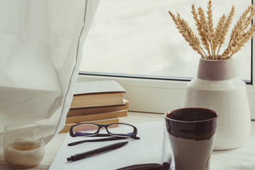 A stack of books, cup of coffee, bouquet of kernels, glasses, notebook and pen over a window. Classy attribute of intelligence reading learning. Moody. Fall mood. Autumn reading